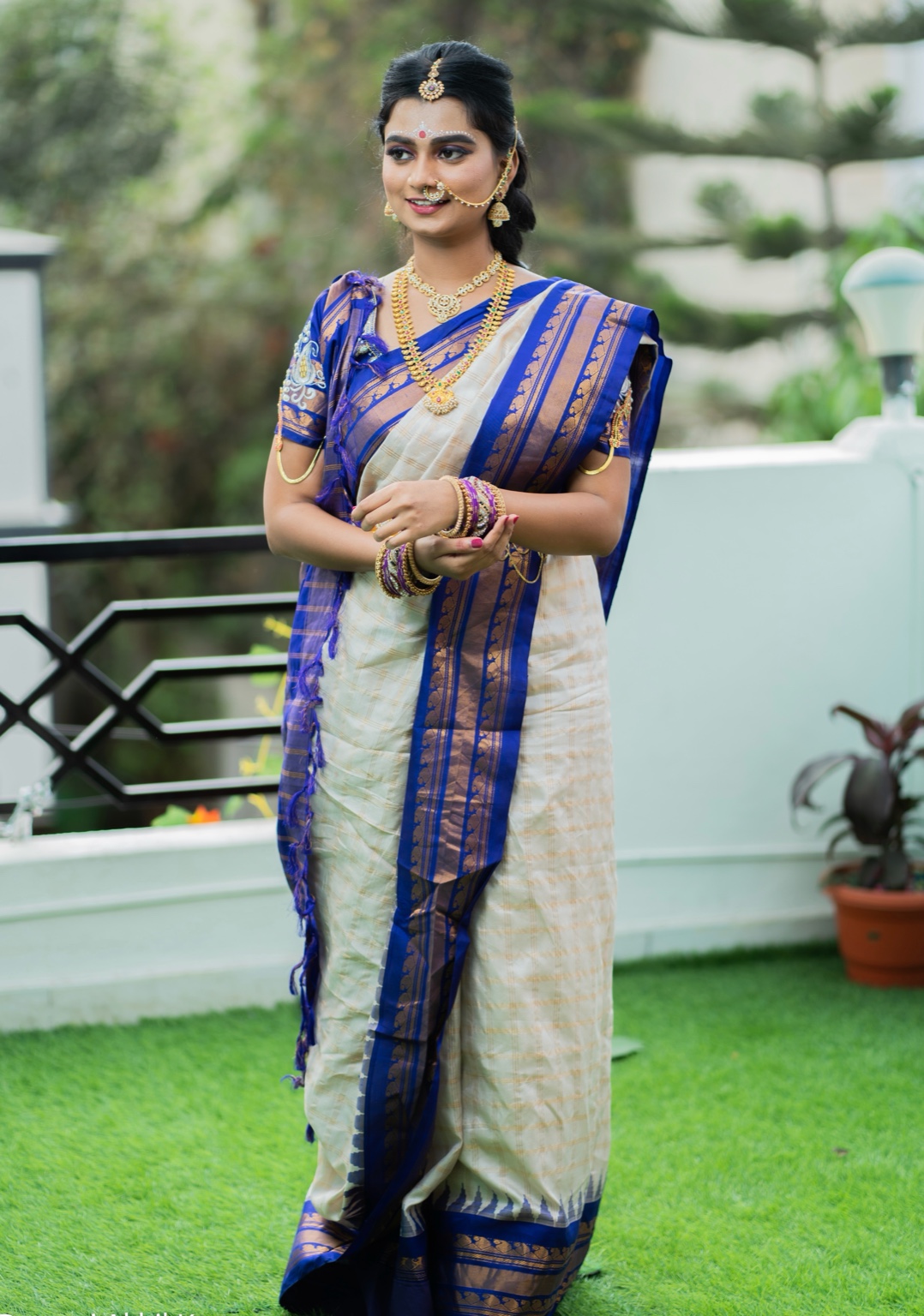 Maharashtrian woman in a white and blue saree with gold jewellery standing outdoors