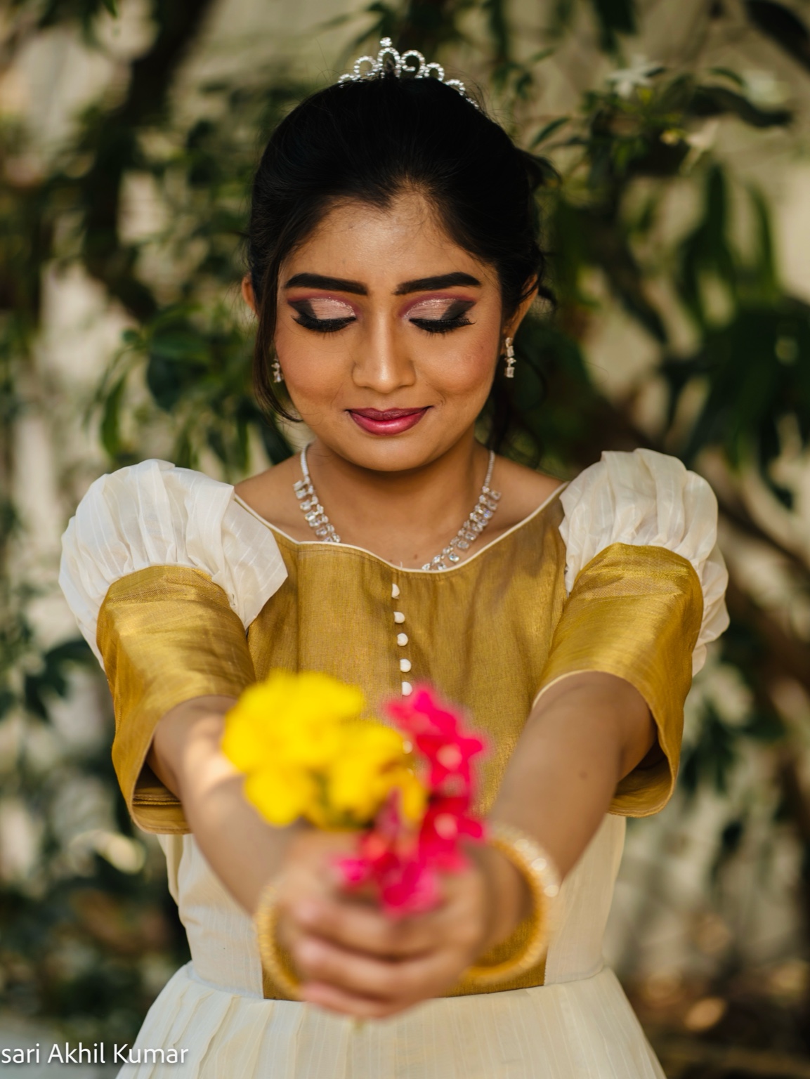 Woman in gold and white gown holding flowers and wearing a tiara