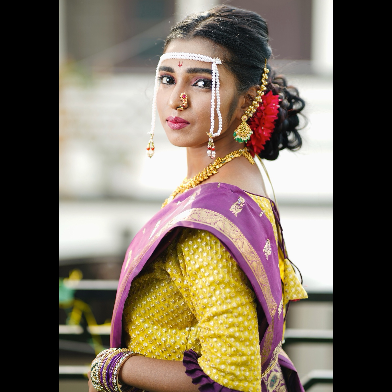 Side profile of a Maharashtrian bride wearing a yellow blouse and purple saree with traditional jewellery