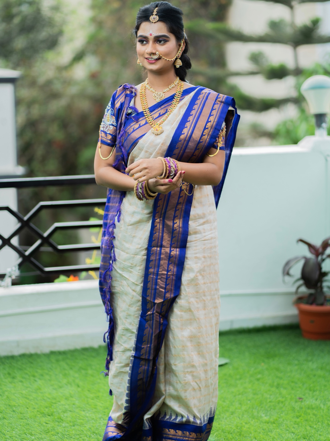 Bride wearing a cream and blue sari with gold jewellery standing outdoors