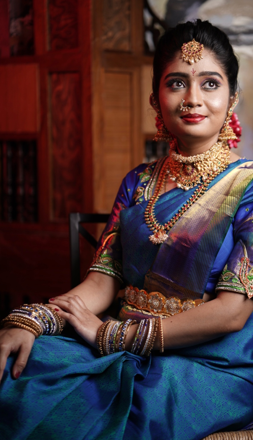 Full length seated portrait of a bride in a blue sari with arms adorned in bangles