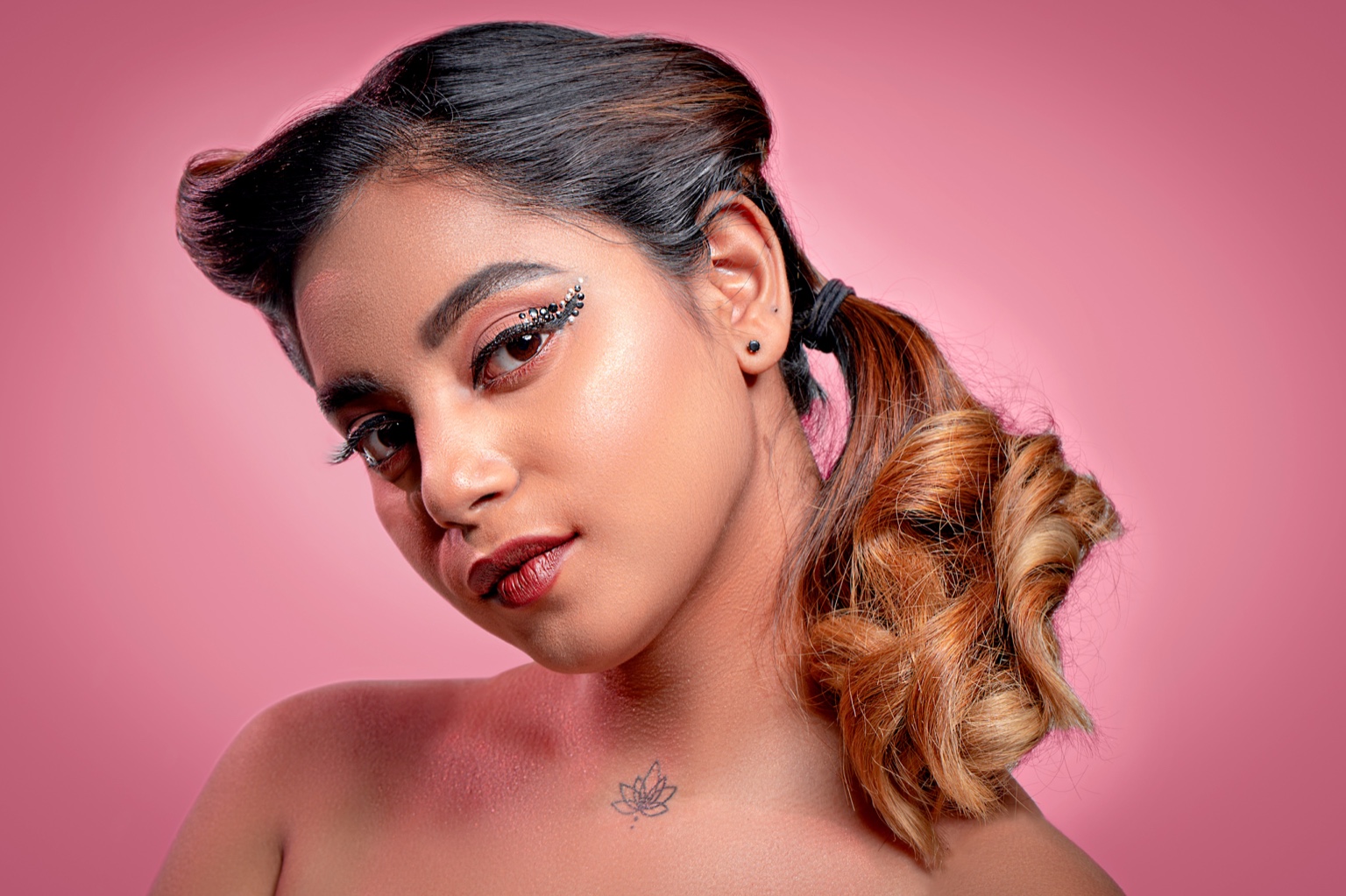 Woman with jeweled eyeliner and curled ponytail against a pink backdrop